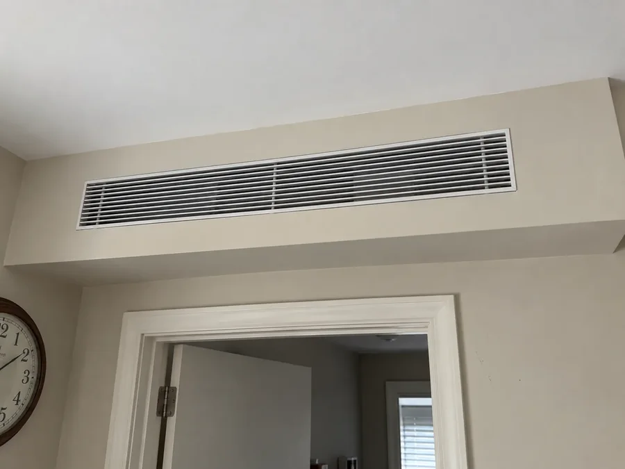 A long slim grille set high on the wall above a doorway, the unit ducted out of sight behind it