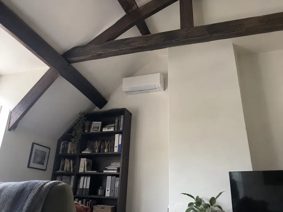 Living room corner with dark exposed beams, the unit fitted on the white wall between them